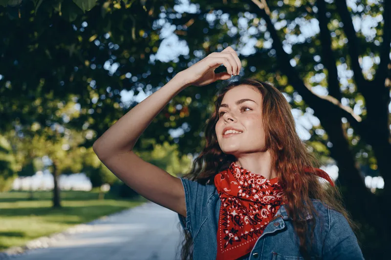 lifestyle woman in modern boho-western denim street style with red bandana enjoying sunny outdoor urban park in film color