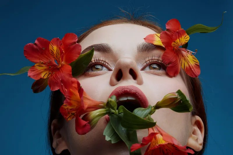 A close up portrait of a young woman with floral arrangements, emphasizing emotions of beauty and nature, featuring vibrant colors against a blue background
