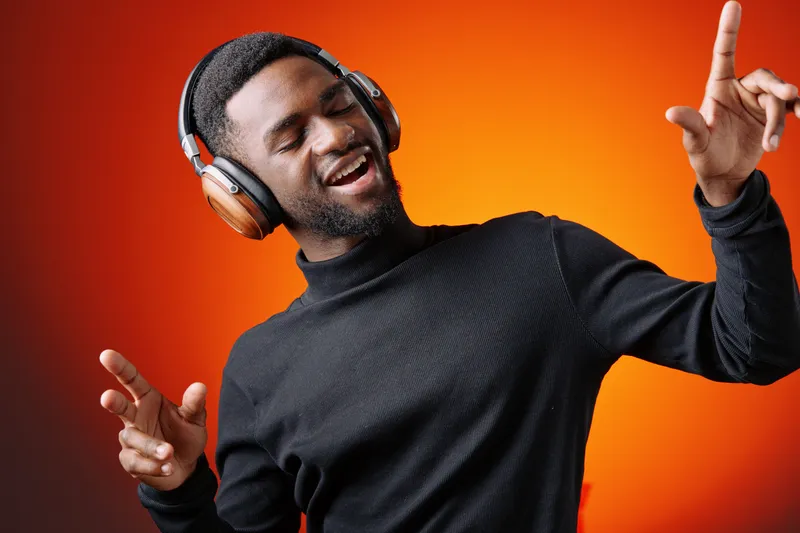 Happy young Black man enjoying music with headphones, dancing against a vibrant orange background, showcasing energy and joy in a modern style