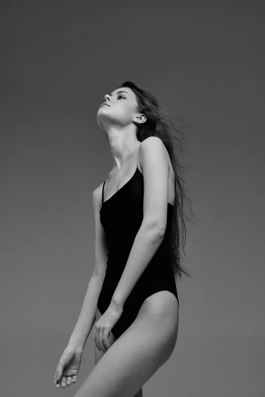 Black and white portrait of a young woman in a swimsuit standing outdoors with a serene expression and natural light.