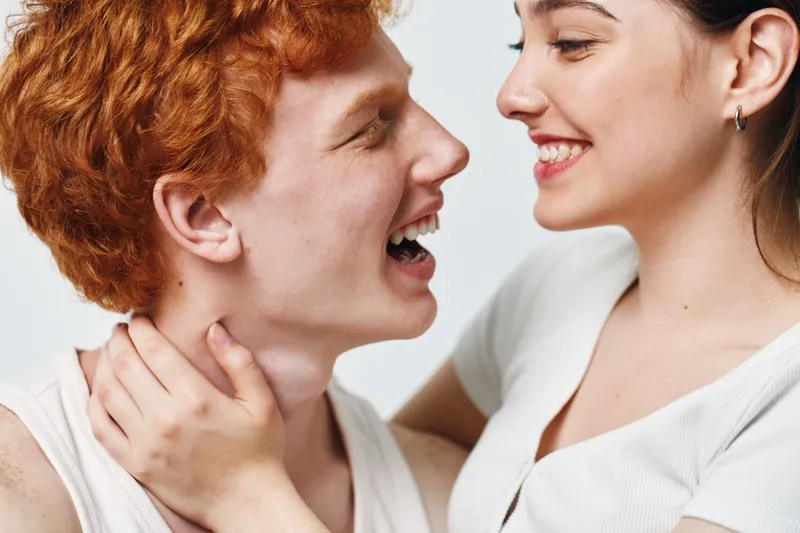 Young couple smiling and looking at each other with affection in bright closeup. Happy woman and man sharing joyful moment in casual clothes and relaxed atmosphere.