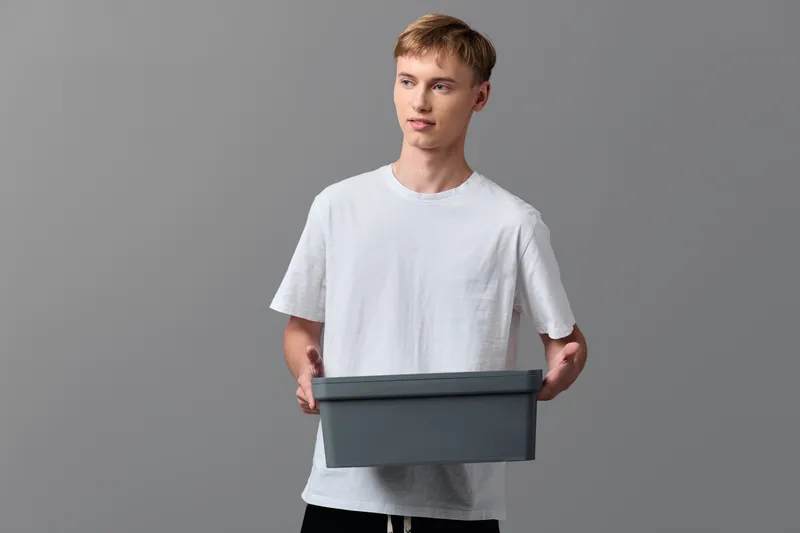 Box holding man in a casual tee presents a clear view of packaging and delivery, illustrating ecommerce order processing and warehouse handling in a modern studio setup with neutral background and