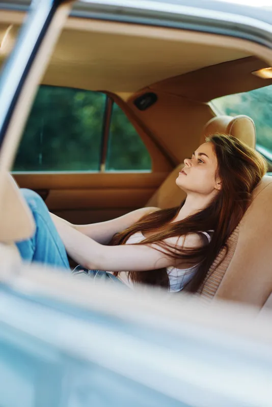 Young woman in casual clothing relaxing in a car cabin, enjoying the serene outdoor view, portraying tranquility and freedom during a summer day.