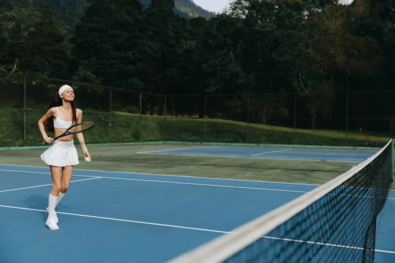 Young female tennis player enjoying a sunny day on the court, wearing a stylish white outfit and radiating joy while holding a racket