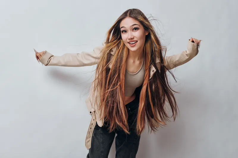 Young woman with long hair smiling and wearing casual jacket and top posing energetically on white background. Teenager, beauty and happiness with natural expression and relaxed style.