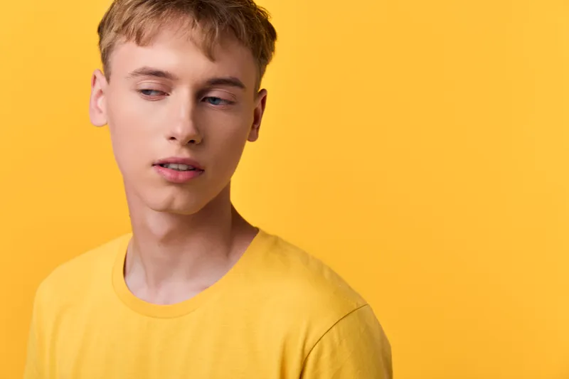 Young man in a yellow shirt stands against a vibrant yellow backdrop, creating a bright, modern studio look with a calm, thoughtful expression and clean minimalist style.