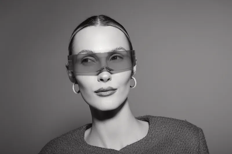 Portrait of a young white woman with pale skin wearing futuristic sunglasses and hoop earrings. Concept of modern fashion, minimalism, and confident style in studio lighting.