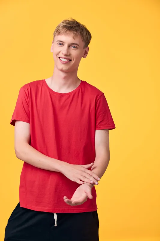 Young man in a red t shirt smiles against a bright yellow background, casual fashion and lifestyle image for advertising, studio lighting, approachable and energetic vibe for campaigns