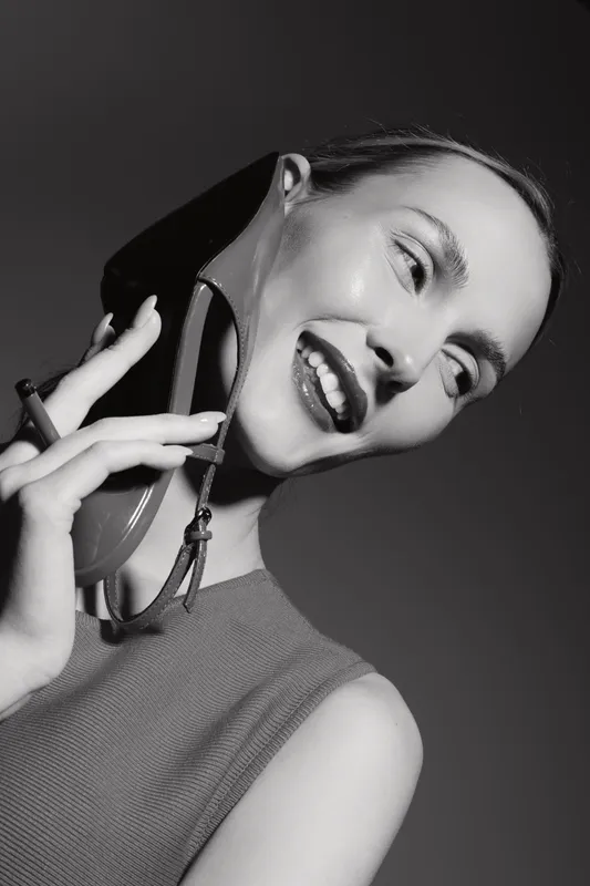 Happy white woman with pale skin smiling holds high heel shoe close to face in studio black and white portrait.