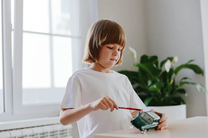 A focused boy engages in creative play, assembling a toy car with precision and curiosity in a bright, inviting room.
