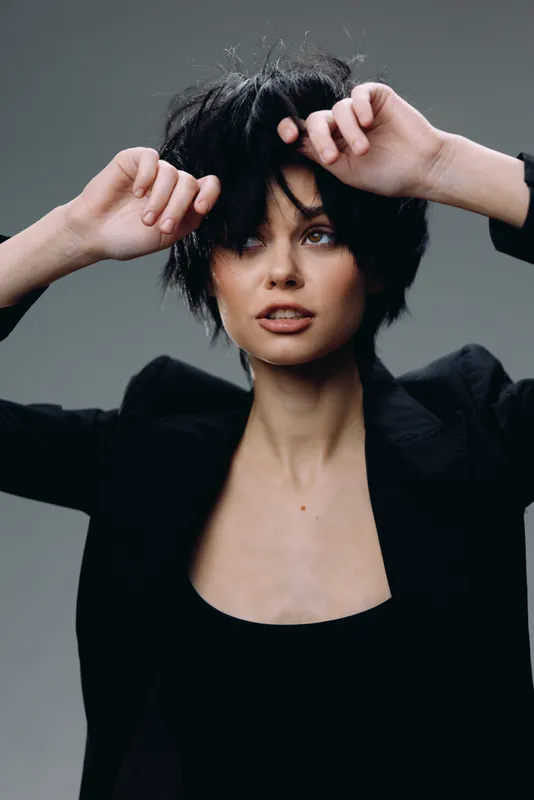 thoughtful woman with short dark hair wearing black jacket in studio setting, expressive face and stylish look
