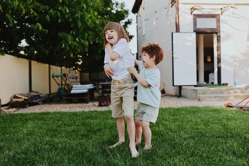 Joyful boys playing together in a sunny garden, outdoors, laughing and having fun, showcasing a carefree childhood experience and vibrant energy.