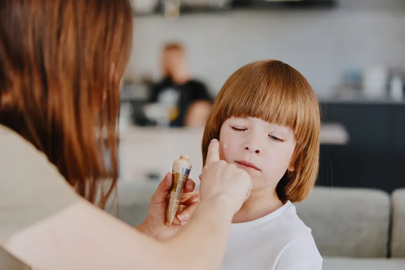 Caring woman applying makeup on a young girl, capturing a tender moment of beauty and creativity in a cozy interior setting, showcasing artistry and affection.
