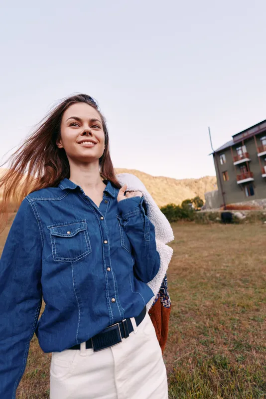 Woman smile denim outdoors portrait in countryside, casual outfit and confident pose near building, young female enjoying nature with sunlight, relaxed mood and modern rustic style.