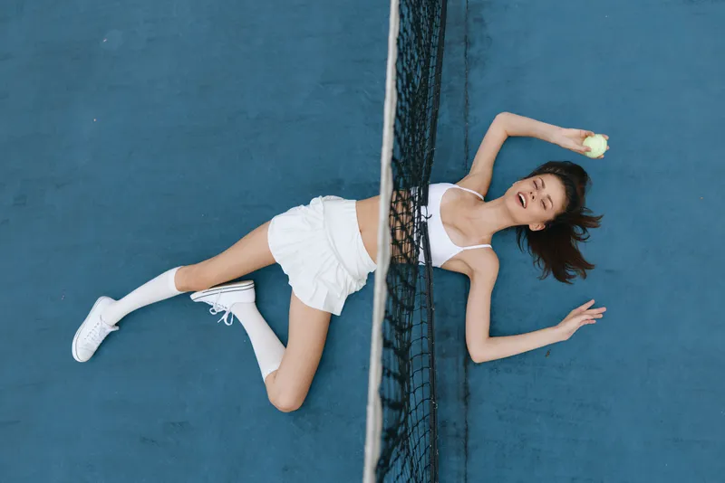 Young female athlete in sportswear laying on a tennis court, expressing joy and relaxation after a match, showcasing active lifestyle and healthy sports concept