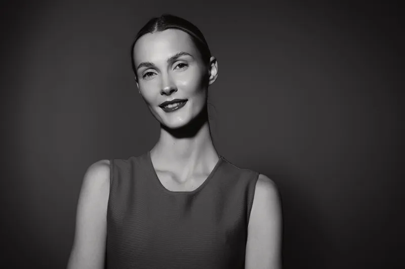 Portrait of a smiling caucasian woman with pale skin and brunette hair in a sleeveless top, against dark background with soft lighting. Concept of elegance and confidence.