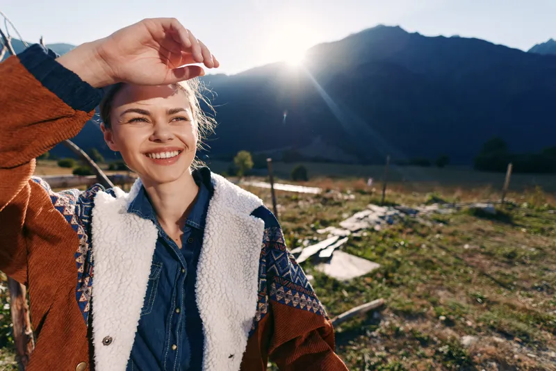 woman smile outdoors mountains sunlight happy portrait of young female traveler wearing warm jacket, enjoying nature hike at sunrise, cheerful expression and scenic valley background