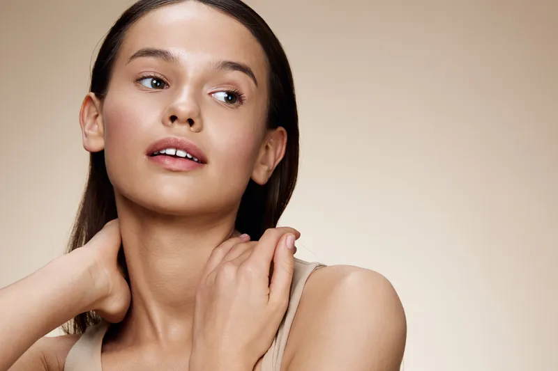 Portrait of a young woman with clear skin and a natural look, showcasing elegant simplicity against a soft, neutral background, embodying beauty and confidence