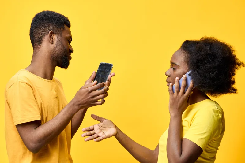 Young African couple communicating with smartphones in vibrant yellow clothing against a yellow background, expressing modern relationship dynamics
