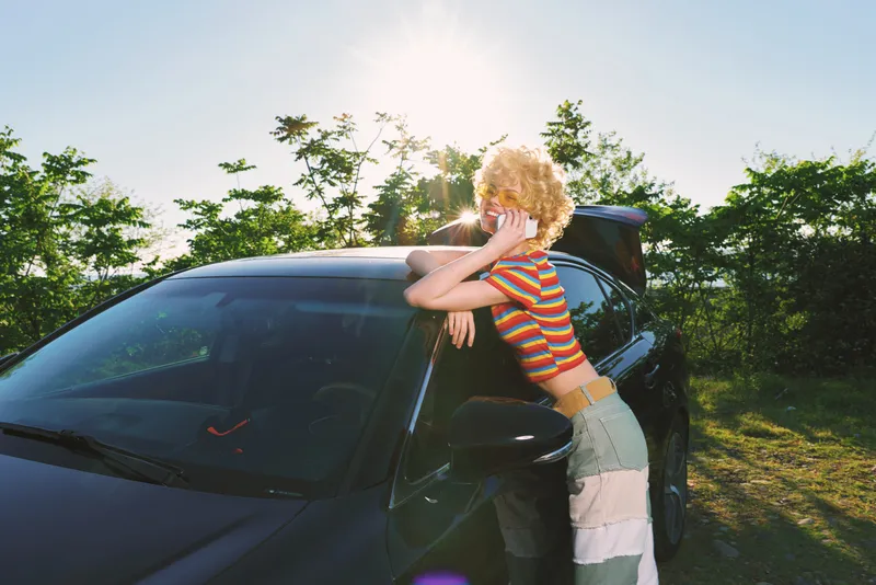Woman leans on a sleek car in bright sunlight, striped shirt, casual denim skirt, outdoor lifestyle shot with retro film color and relaxed mood