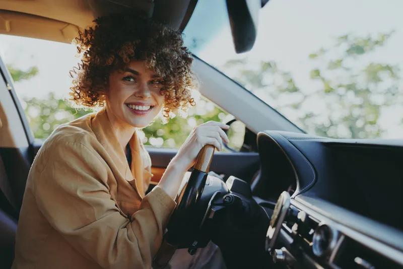 Happy woman driving a car, casual lifestyle portrait with retro film color tones, warm natural light, smiling at the wheel, daylight interior scene, candid moment captured on camera