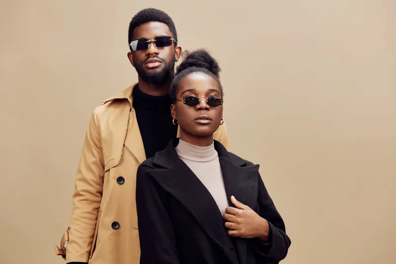 Stylish couple wearing sunglasses, posing confidently against a warm beige background, showcasing modern fashion and urban elegance in a seasonal autumn setting