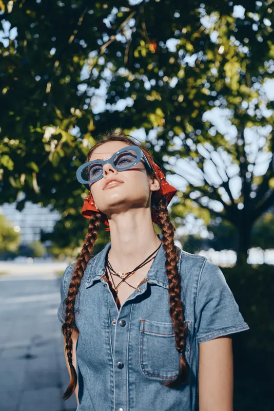 lifestyle woman in modern boho-western denim street style wearing blue sunglasses and red bandana, captured with warm film color outdoors in natural sunlight
