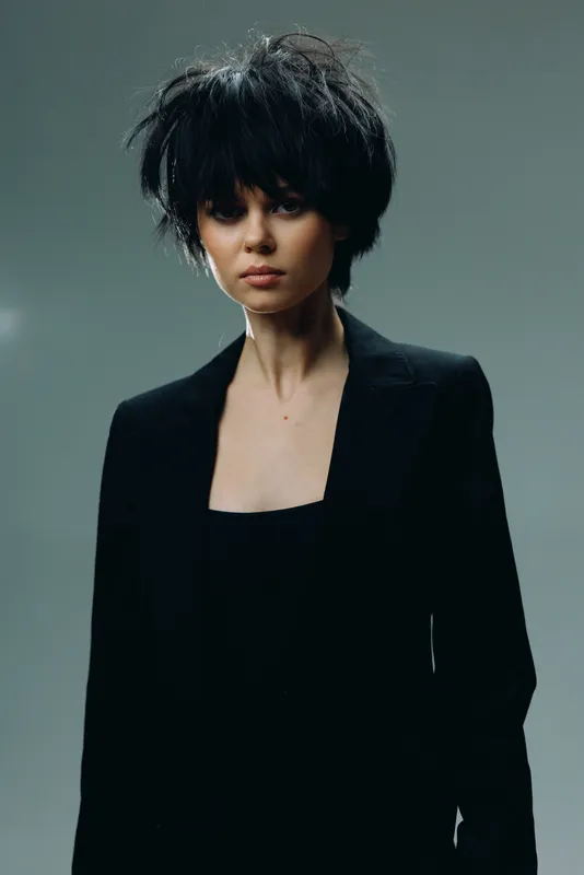 Stylish woman with short dark hair wearing black blazer in moody studio lighting, portrait with serious expression and elegant style
