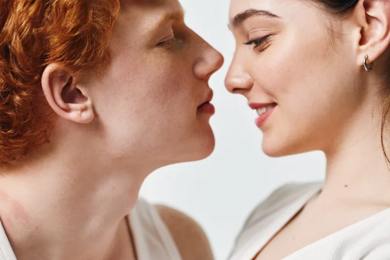 Couple, young man and woman close to each other, intimate moment with gentle expressions and soft lighting on white background. Romance, connection and affection between two people.