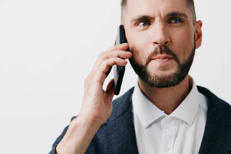 A professional man in a blazer speaks on a smartphone against an isolated colored background, conveying focus, confidence, and a dynamic business mood.