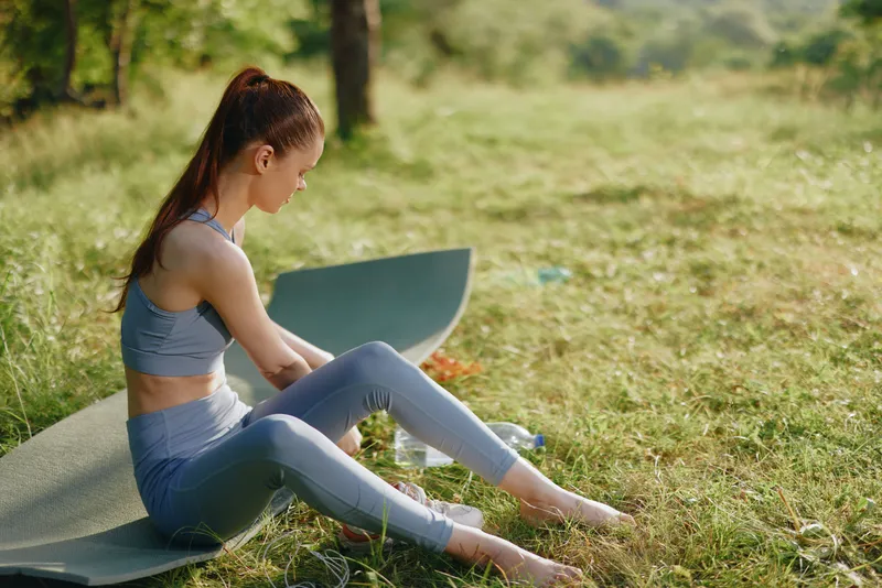 Young woman practicing yoga outdoors in a serene, green environment, wearing stylish athletic gear, embodying tranquility and mindfulness