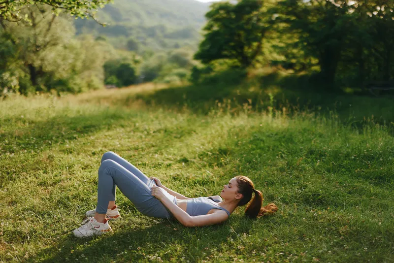 Young woman in athletic wear practicing yoga outdoors in a serene green landscape, showcasing relaxation and tranquility during a sunny day