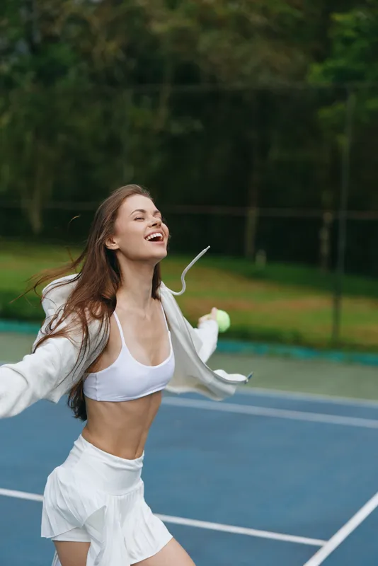 Joyful young female athlete celebrating victory on a tennis court, wearing sports attire and displaying emotions of happiness, excitement, and determination