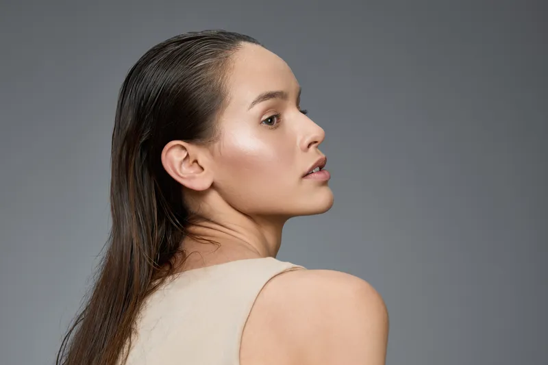Elegant portrait of a model with wet hair, showcasing natural beauty and soft skin tones against a neutral background, perfect for beauty and fashion concepts