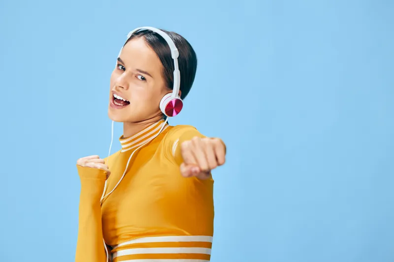Vibrant woman in a bright orange athletic top wearing headphones shows energetic fitness movement, active sport vibe, and upbeat mood in a clean studio backdrop, perfect for wellness campaigns and
