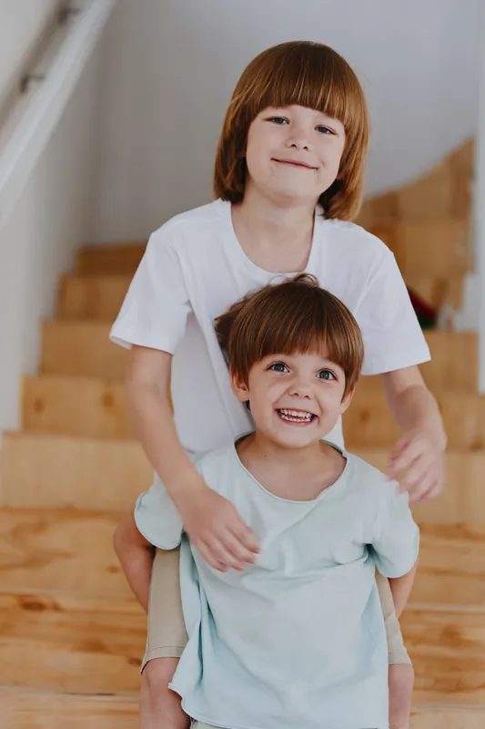 Smiling brothers joyfully playing together on wooden stairs, showcasing their bond and happiness in a bright and cheerful environment.