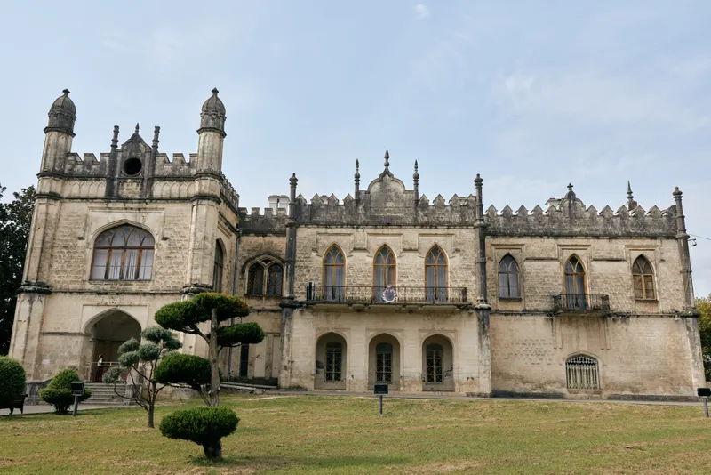 Historic castle like building with ornate stonework and towers on a manicured lawn, presenting grand architecture and a medieval atmosphere.