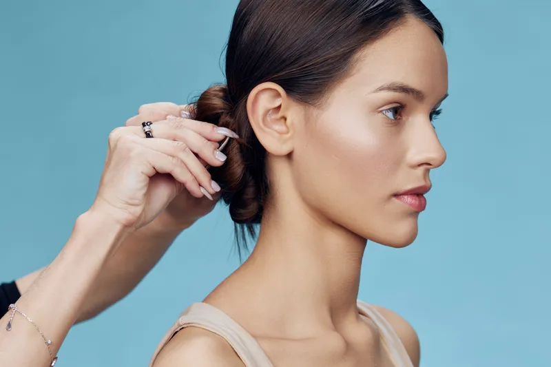 A young woman with a professional hairstyle being styled against a soft blue background, showcasing beauty and elegance in a modern setting