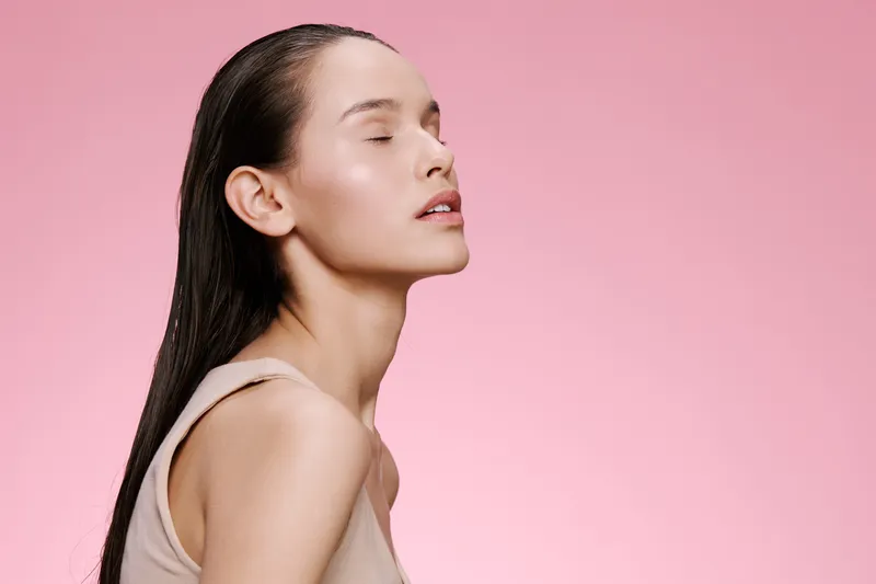 Serene young woman with wet hair against a soft pink background, embodying beauty and confidence in a minimalistic style Ideal for beauty and skincare concepts