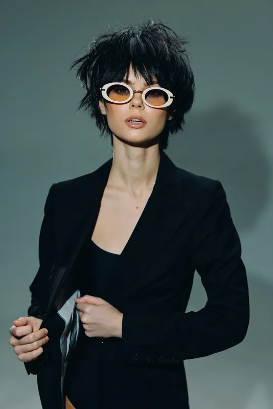 Stylish woman wearing black blazer and retro sunglasses with short black hair in studio lighting
