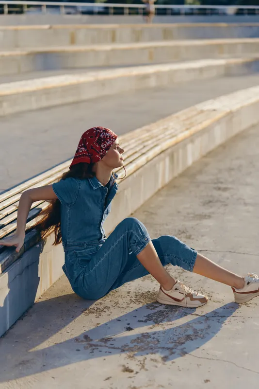 lifestyle woman in modern boho-western denim street style wearing a red bandana sits relaxed on urban steps in warm natural light, film color aesthetic