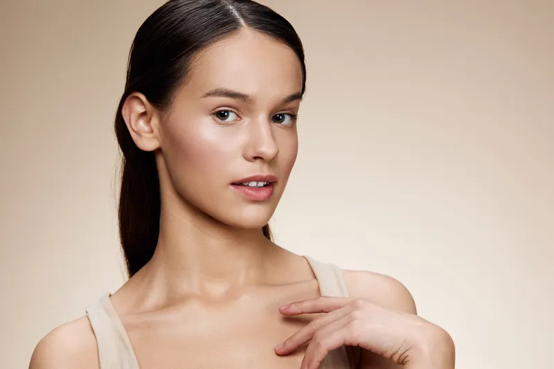 Young woman with natural beauty, wearing simple clothing, showcasing clear skin and calm expression against a neutral background