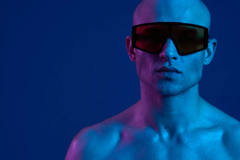 Stylish man in sunglasses, showcasing bold colors with vibrant lighting, creating an eye-catching portrait against a rich blue backdrop.