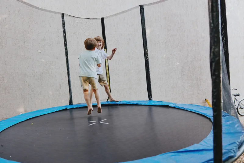 Two happy children jumping on a trampoline, enjoying outdoor play in a sunny setting, showcasing joyful moments and energetic fun.