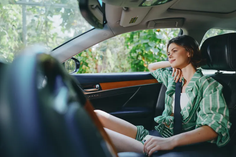 A young woman sits inside a modern car, relaxed in a casual green striped shirt, sunlight streaming through the window, a calm, intimate moment.
