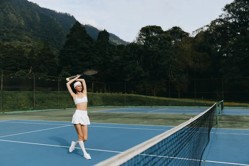 Young athletic woman in white sportswear playing tennis outdoors, demonstrating joy and energy on a sunny day, ideal for sports lifestyle and fitness themes