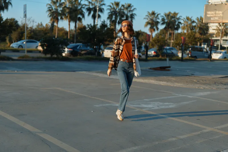 Woman walking in a parking lot at golden hour with palms and casual outfit, smile and denim jacket. Candid lifestyle portrait emphasizing authenticity, golden hour glow, emotional storytelling,