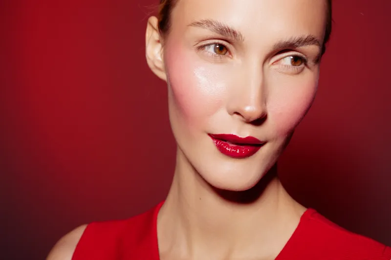 Close-up of a woman with red lipstick and blush wearing a red top against a red background. Concept of beauty, makeup, fashion, and confident female portrait.