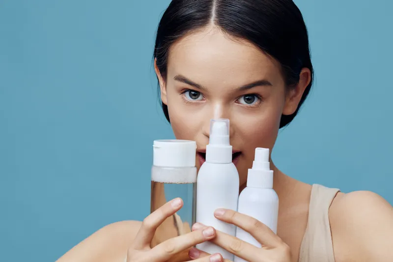 Young woman showcasing skincare products against a light blue background, emphasizing beauty and self care, with a focus on natural ingredients and healthy skin
