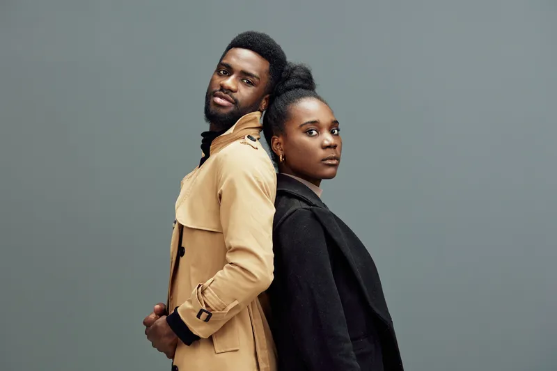 Stylish African American couple posing back to back in fashionable coats against a gray background showcasing contemporary fashion and confidence